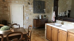 A rustic kitchen with stone walls, wooden cabinets, a white sink, and a dining table with chairs.