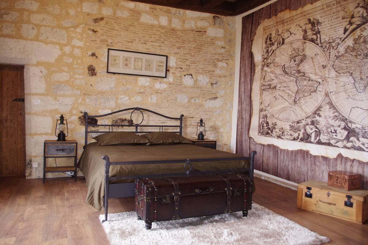 Ein Schlafzimmer mit einer Steinsturz, einer großen Karte, einem Bett, einer hölzernen Bank und zwei Nachttischen mit Lampen.