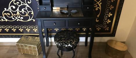 A black desk with drawers, a small stool, and two bottles labeled 'HOTEL DE PARIS'.