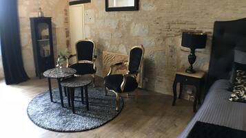A room with a stone wall, a bed, a round table with chairs, a small cabinet, and a framed picture on the wall.