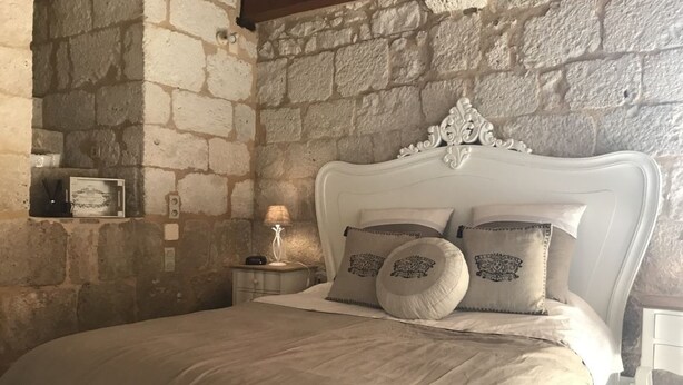 A bedroom with a stone wall, a white ornate headboard, and a bed with beige bedding and decorative pillows.