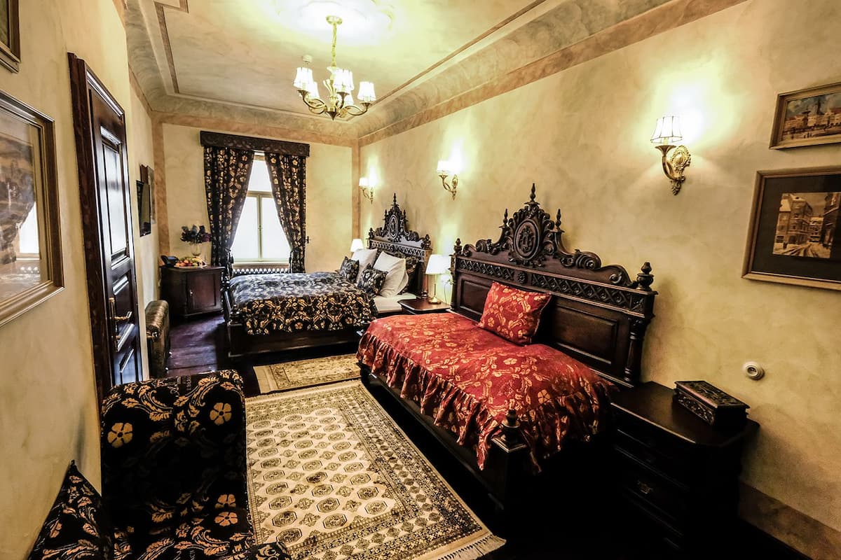 A hotel room with two beds, a chandelier, wall sconces, and a large window with curtains.