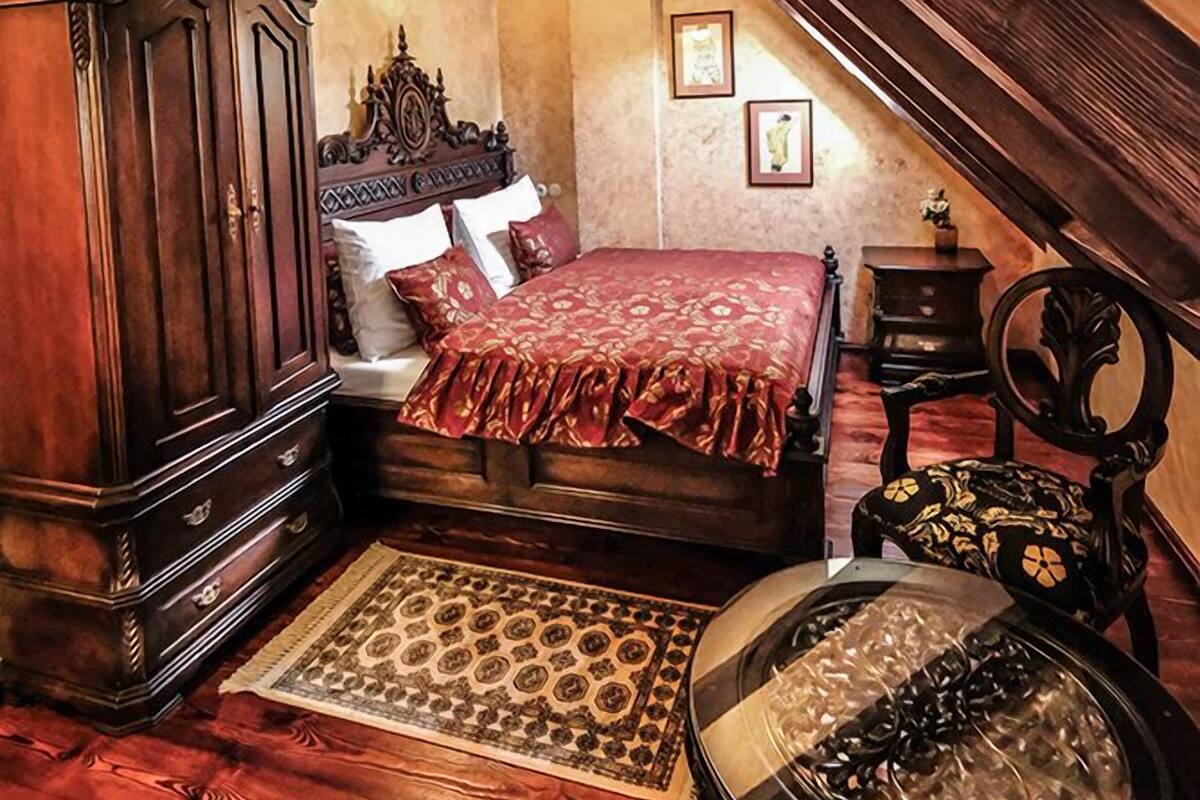 A bedroom with a wooden bed, a chest of drawers, a small table, and a decorative chair.