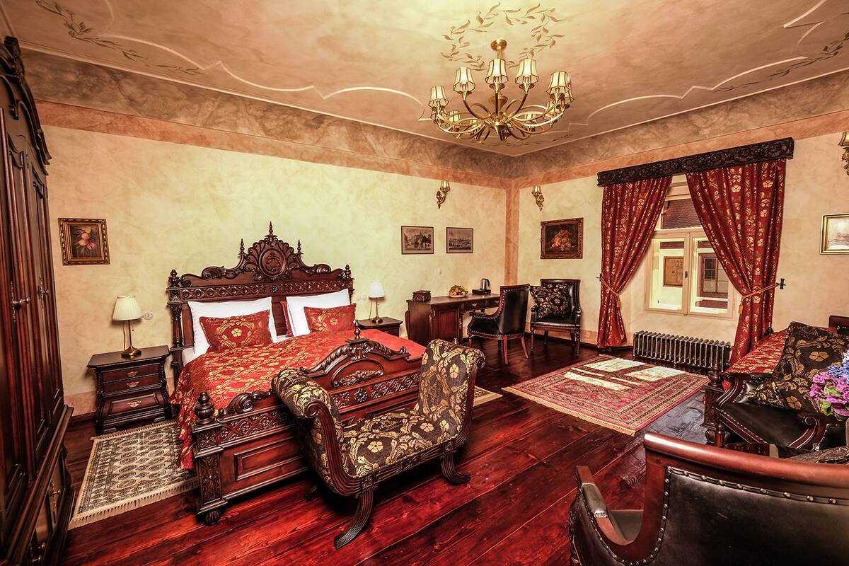 A traditional room with a large ornate bed, a wooden floor, a chandelier, and classic furniture.