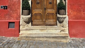 Un edificio de piedra con un gran portón de madera, una ventana pequeña y una maceta a cada lado.