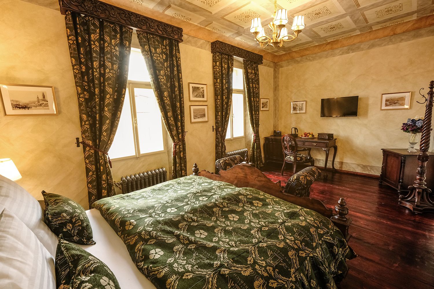 A classic room with a large bed, two chairs, a desk, and a television.