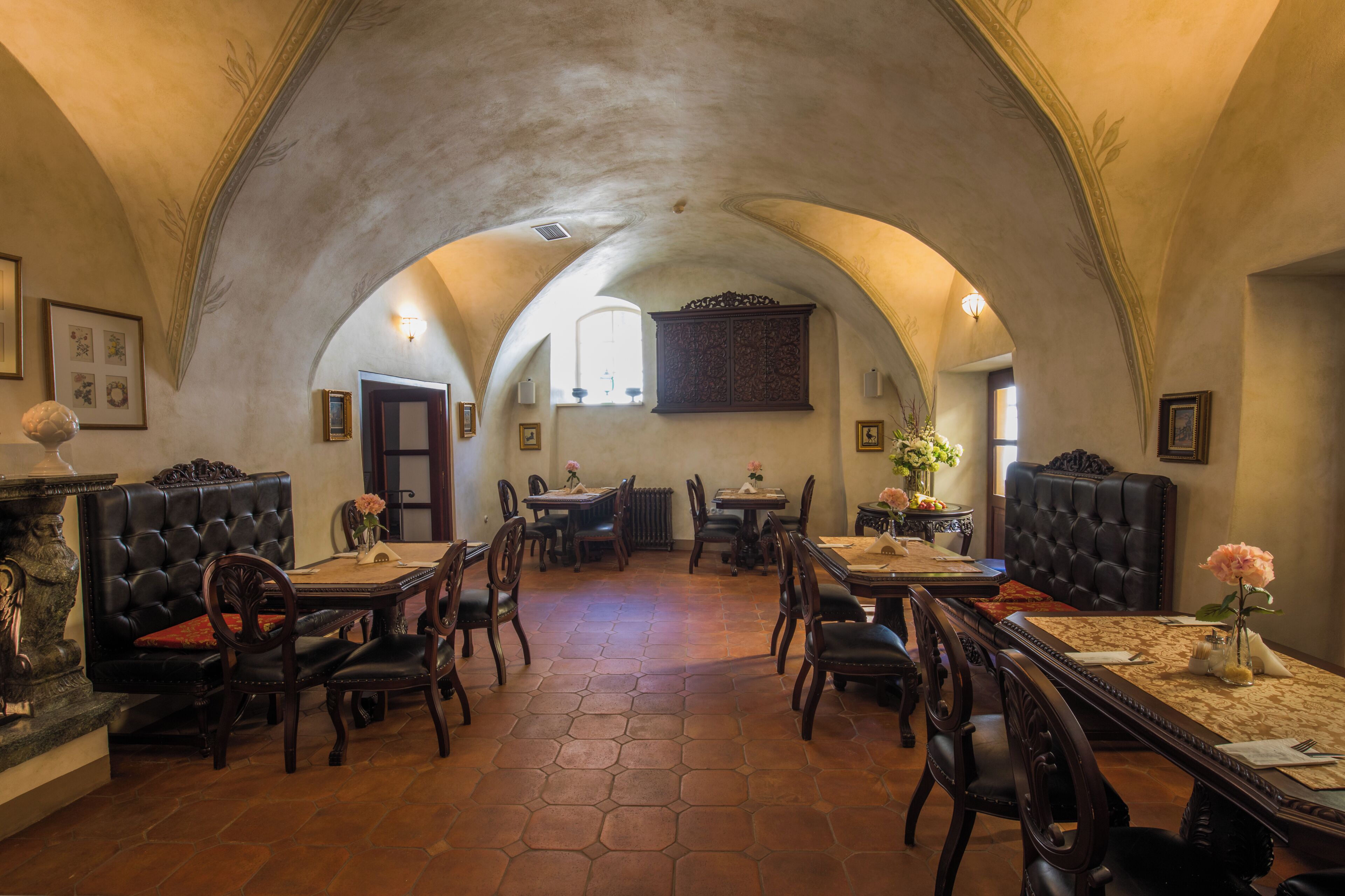 Un interior con techos abovedados, una zona de comedor central con mesas y sillas, y una chimenea con un cojín rojo.
