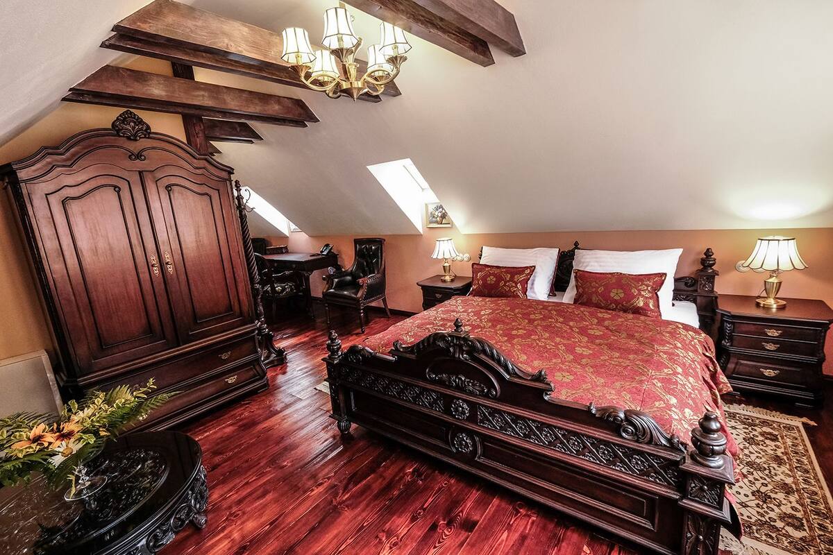 A bedroom with a large bed, wooden wardrobe, and a desk.