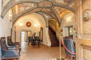 Un interior con una imponente escalera, techo ricamente decorado y zona de estar.
