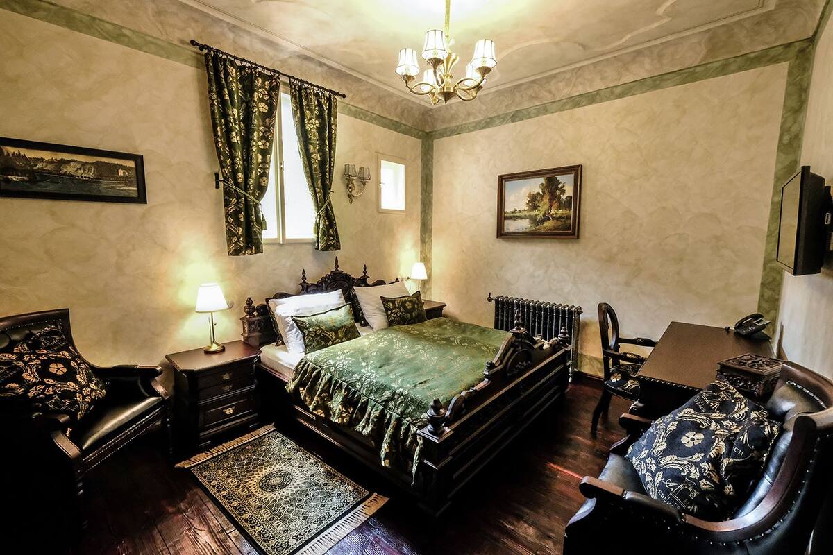 A traditional bedroom with a four-poster bed, two bedside tables, a desk, and a chair.