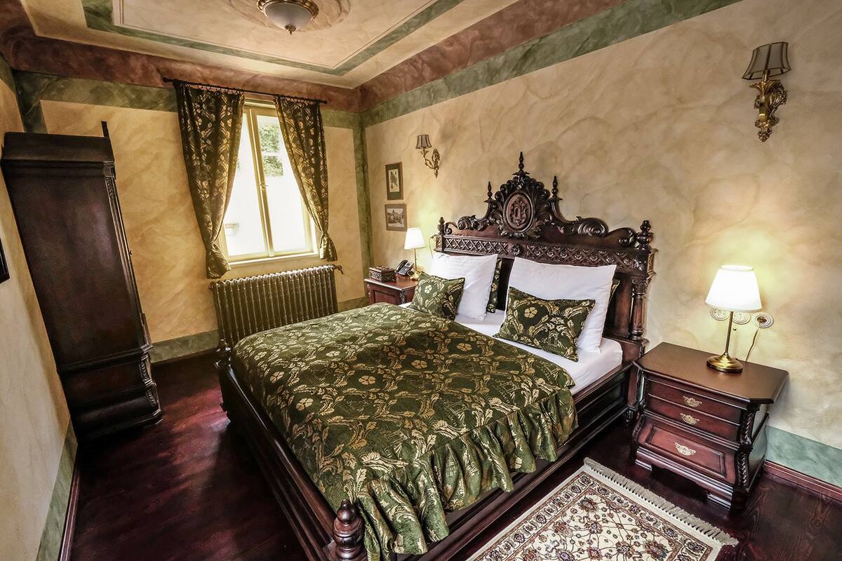 A traditional bedroom with a large bed, a wooden dresser, a nightstand, and a lamp.