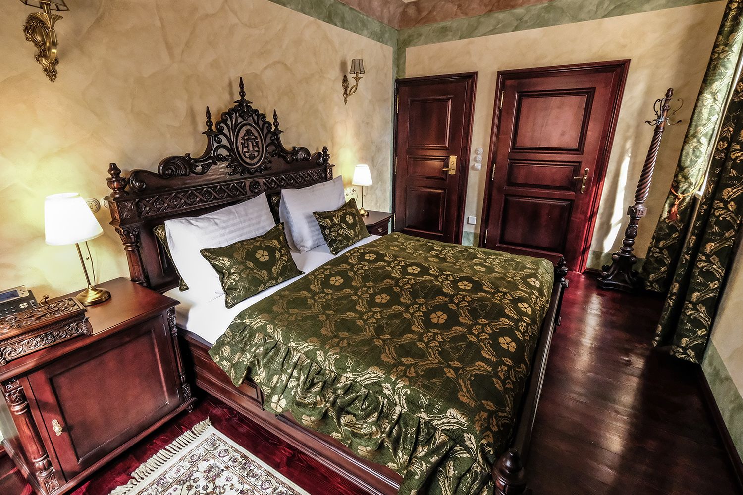 A traditional bedroom with a large bed, two bedside tables, a nightstand, a mirror, and two doors.