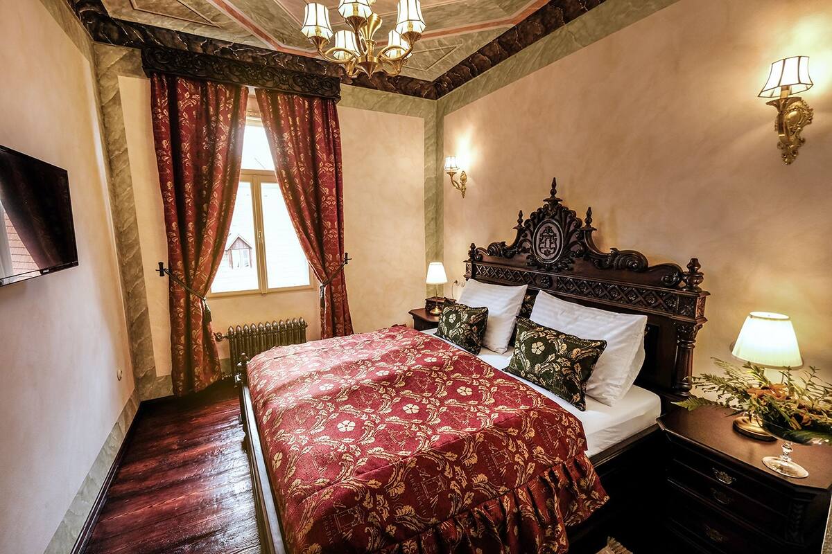 A bedroom with a large bed, ornate headboard, and a chandelier.
