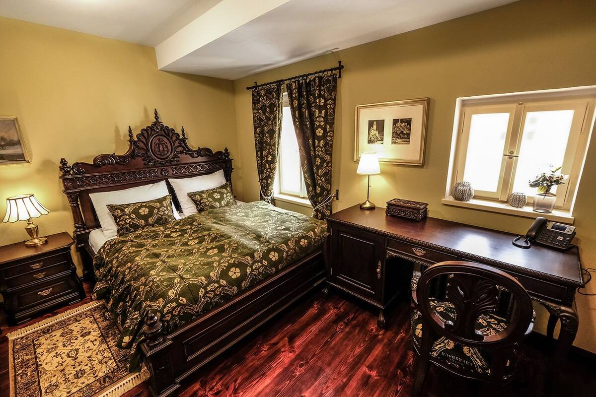A traditional bedroom with a four-poster bed, a desk with a telephone, and a chair.