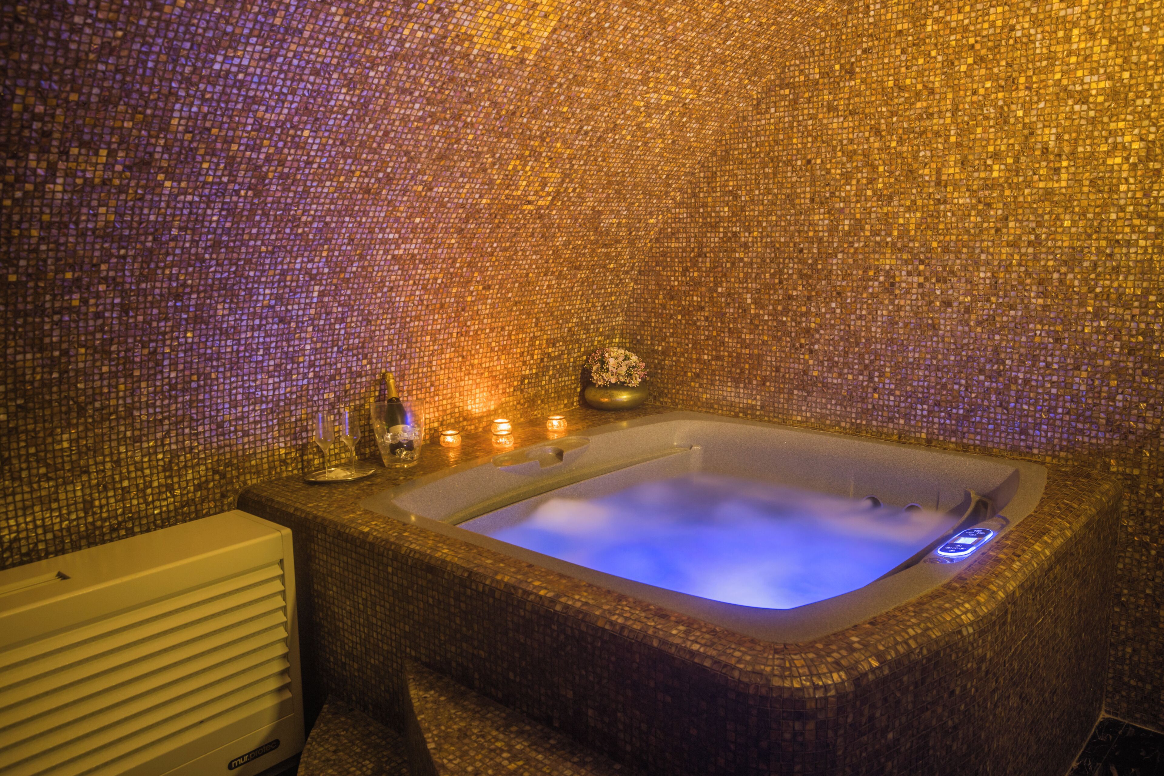 Un jacuzzi con paredes de mosaico, un radiador blanco y velas.