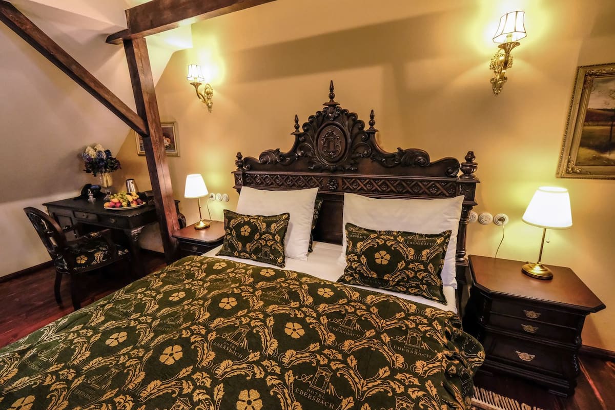 A hotel room with a large bed, two bedside tables, a desk with a chair, and a lamp.