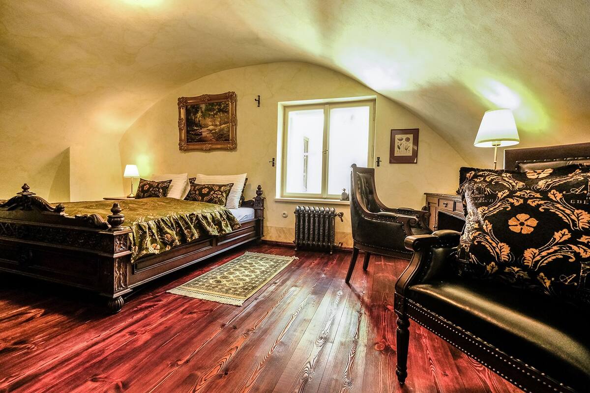 A bedroom with a wooden bed, a chair, a sofa, a radiator, and a window.