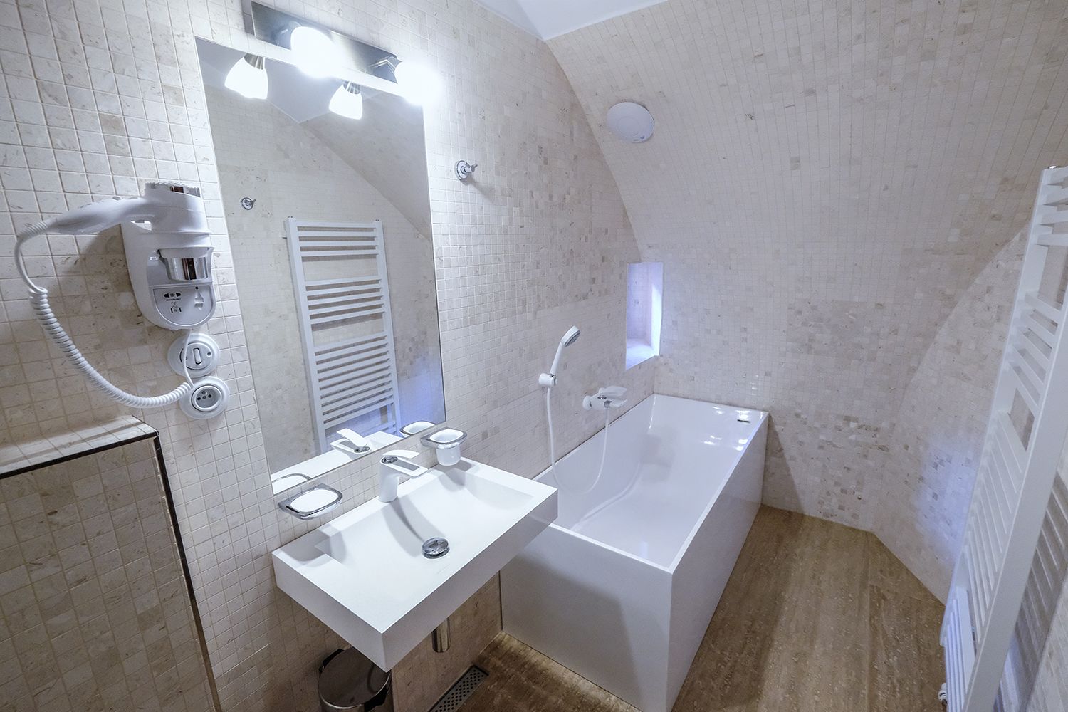 A modern bathroom with a white sink, mirror, and bathtub. There is a hairdryer on the wall and a towel rack.
