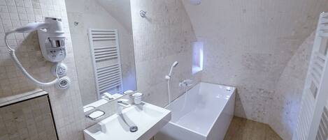 Un baño moderno con lavamanos, espejo y bañera blancos. Hay un secador de pelo en la pared y un perchero para toallas.
