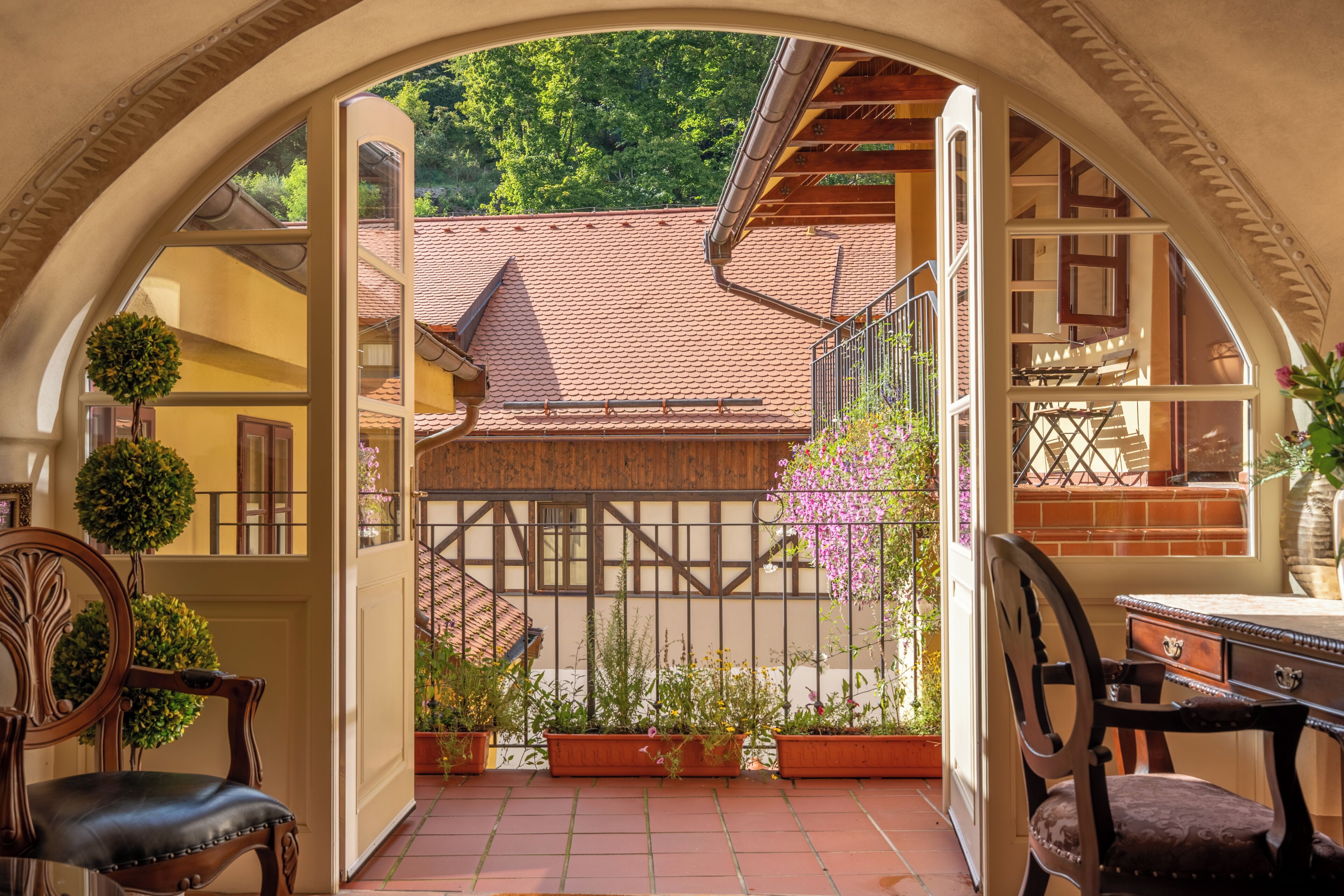 An arched entrance to a courtyard with a tiled floor, wooden furniture, and potted plants.