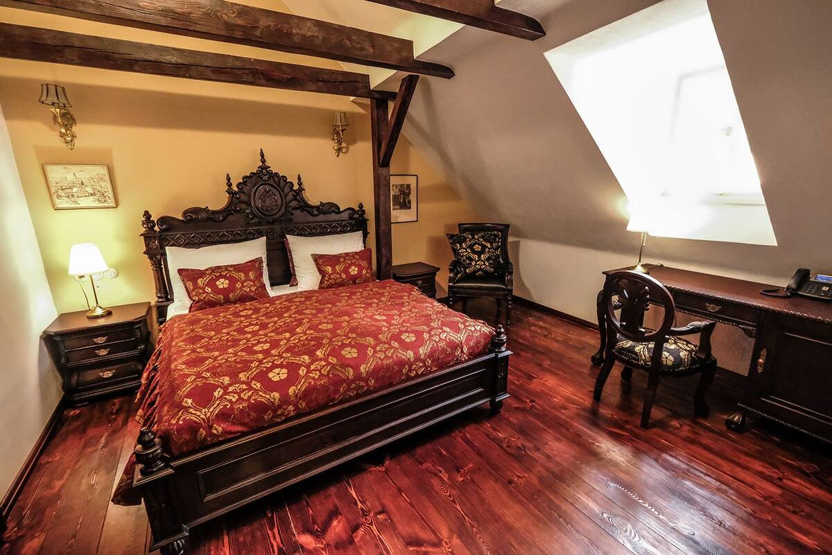 A bedroom with a large bed, wooden headboard, two nightstands, a desk, and a chair.