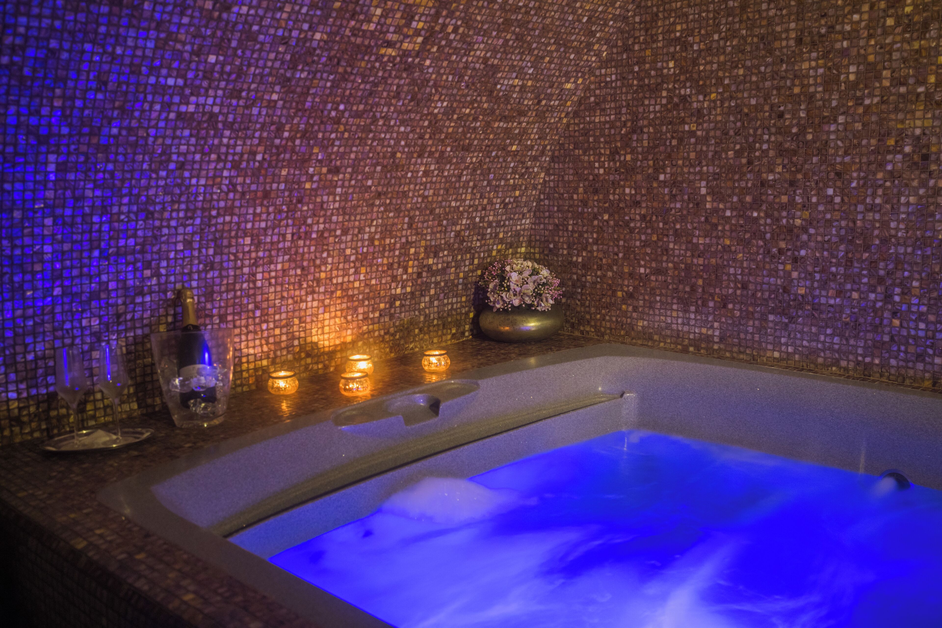 A hot tub with a mosaic wall, candles, and a bouquet of flowers.