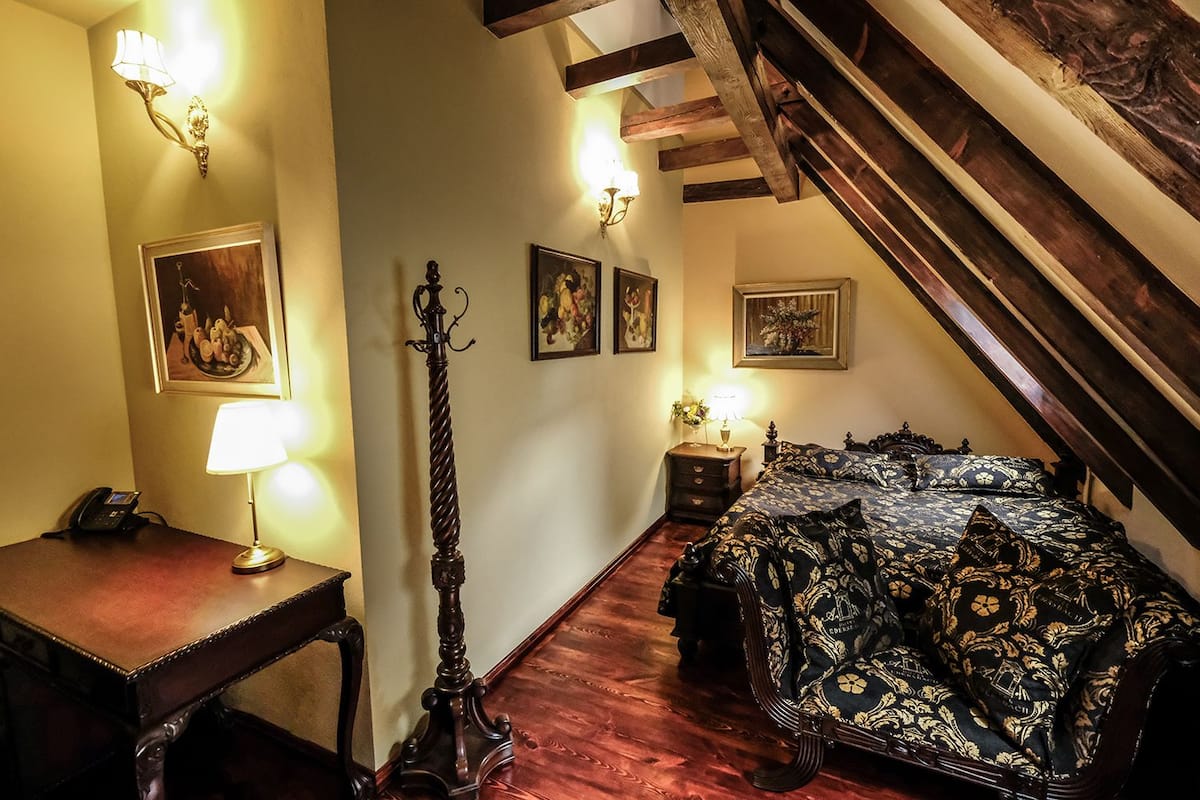 A bedroom with a wooden bed, a desk with a lamp, a telephone, and framed artwork on the walls.
