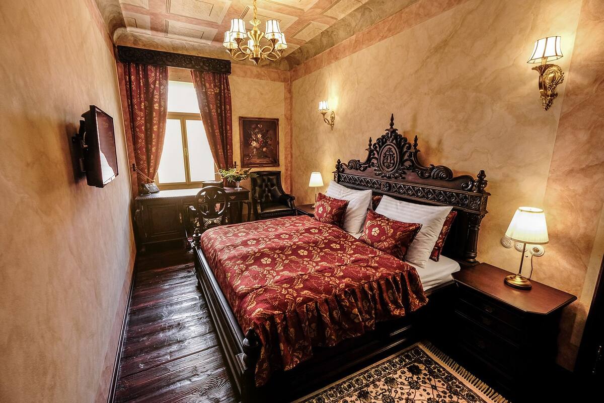 A traditional bedroom with a four-poster bed, ornate wall sconces, and a chandelier.