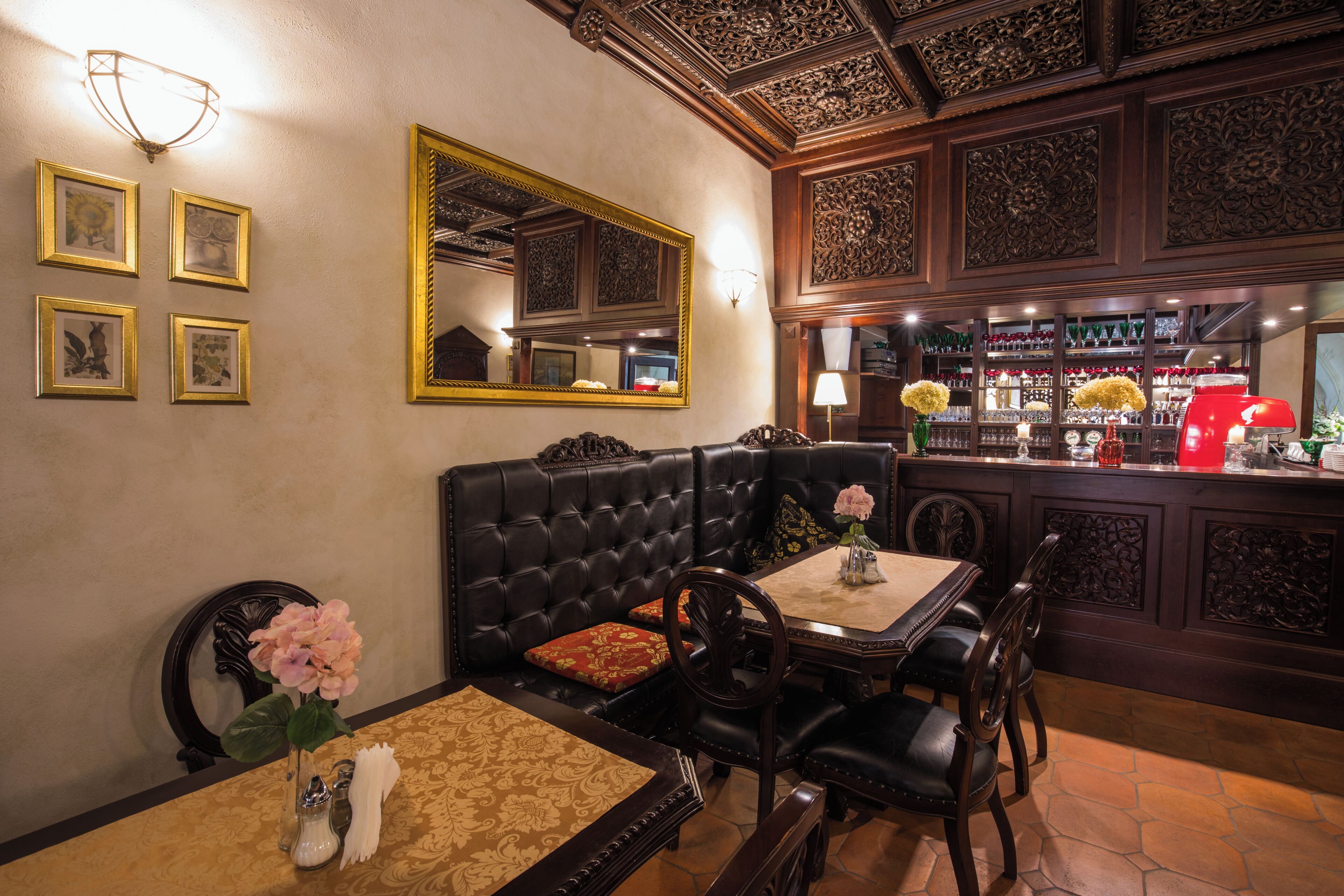 A room with a black leather sofa, a dining table with chairs, a large mirror, and a bar area with shelves of glassware.