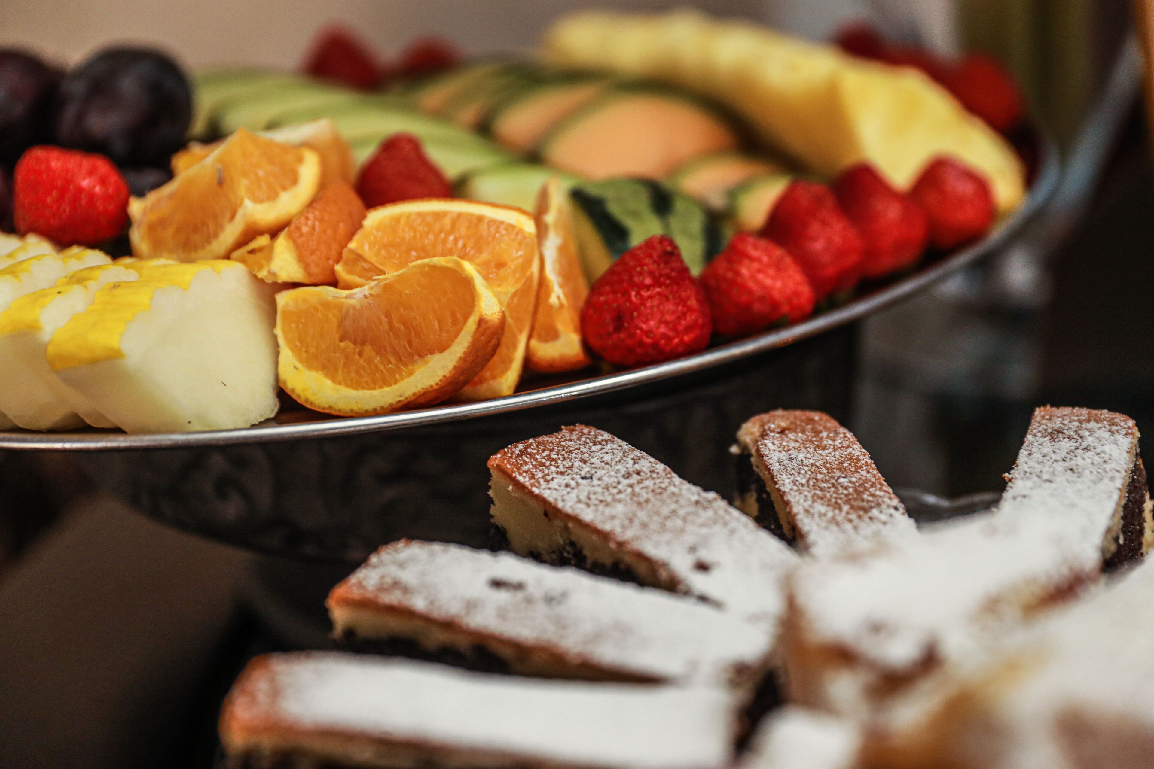 A fruit platter with various fruits and a dessert tray with pastries.