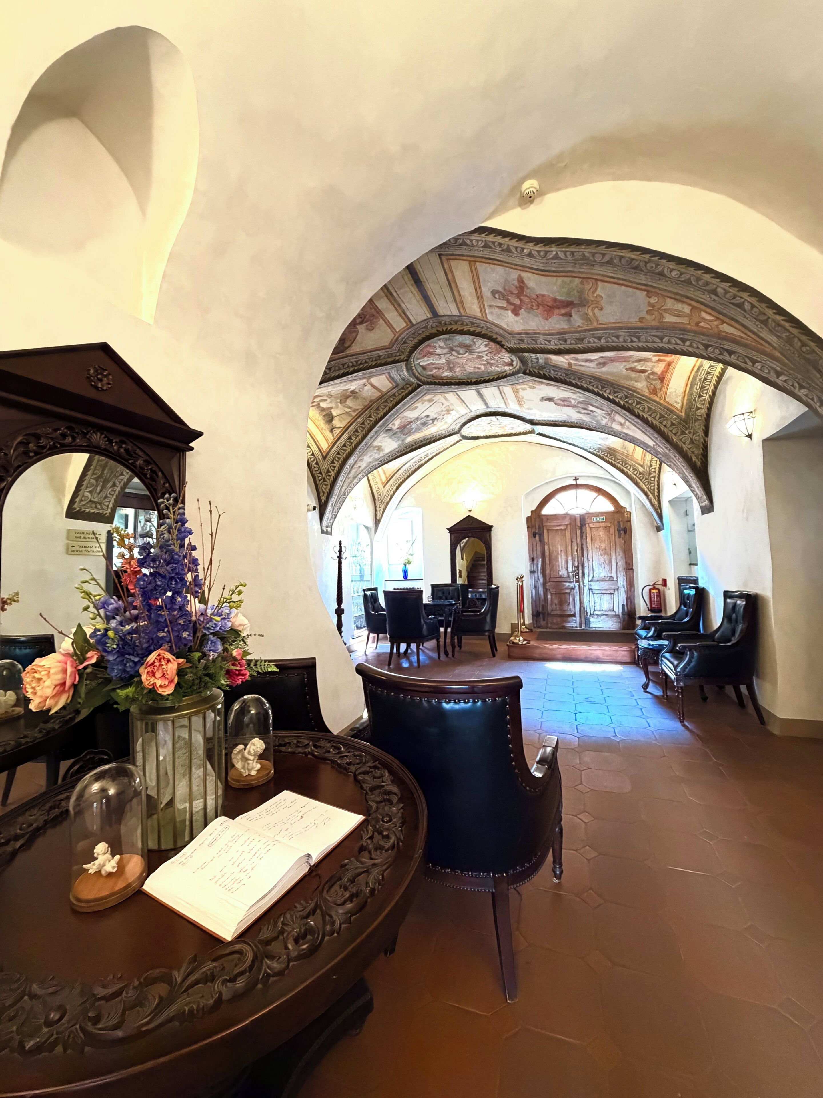 An interior with a dining area, a table with a vase of flowers, and a ceiling with intricate designs.