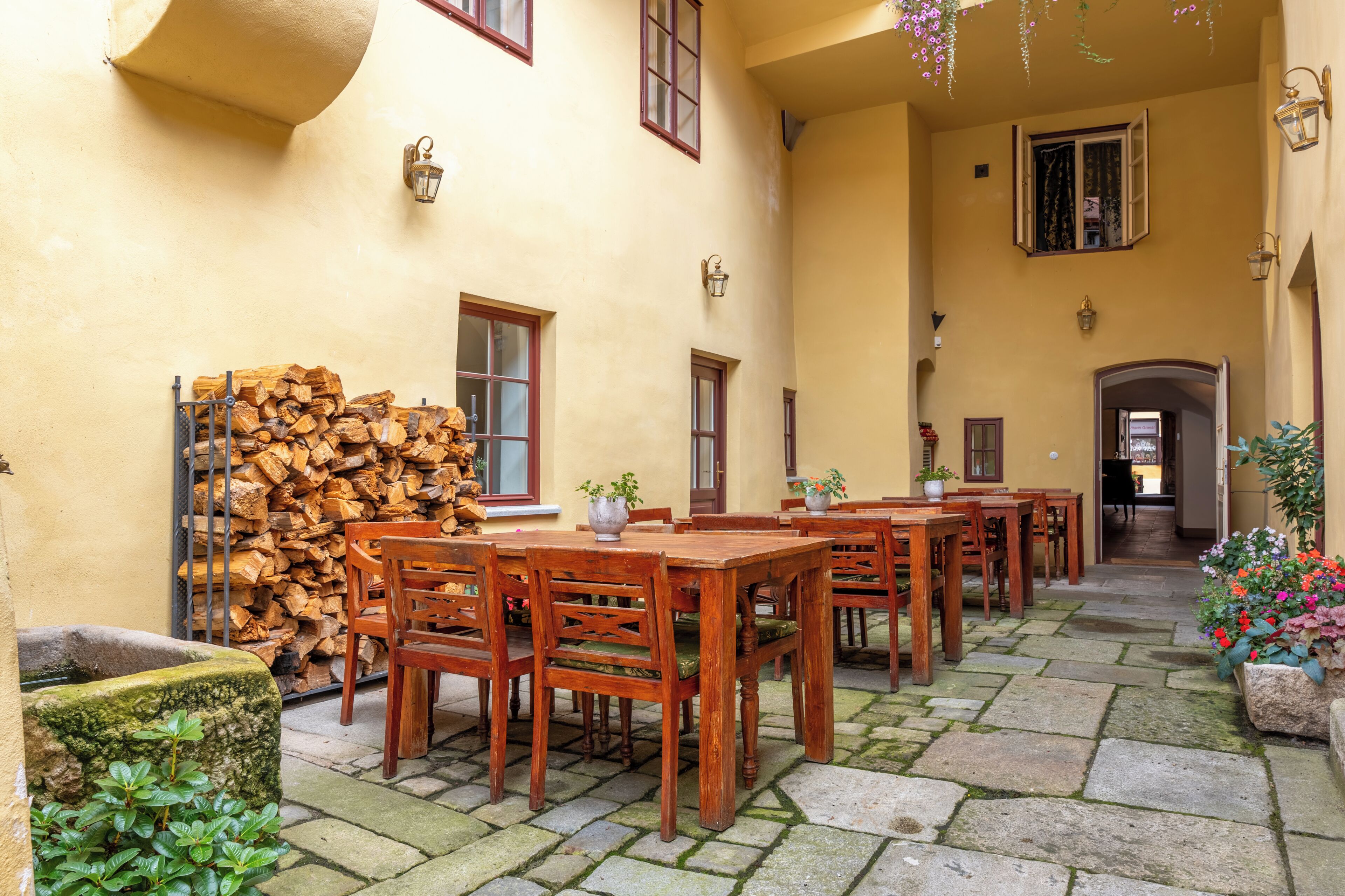 Ein Innenhof mit Holztischen und -stühlen, einem Holzstapel und einem Stebrunnen.