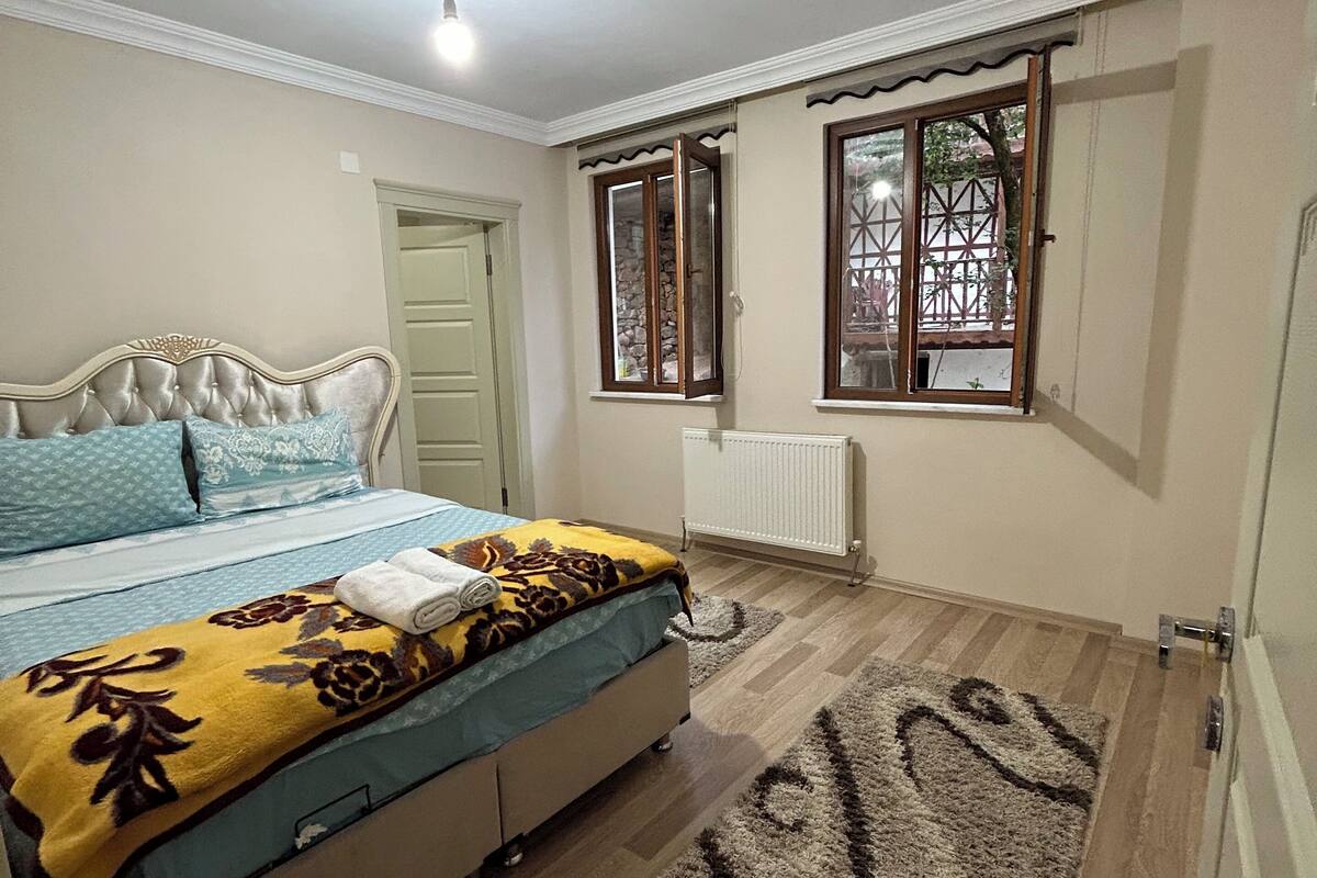 A bedroom with a bed, a radiator, a window with a view, and a ceiling light.