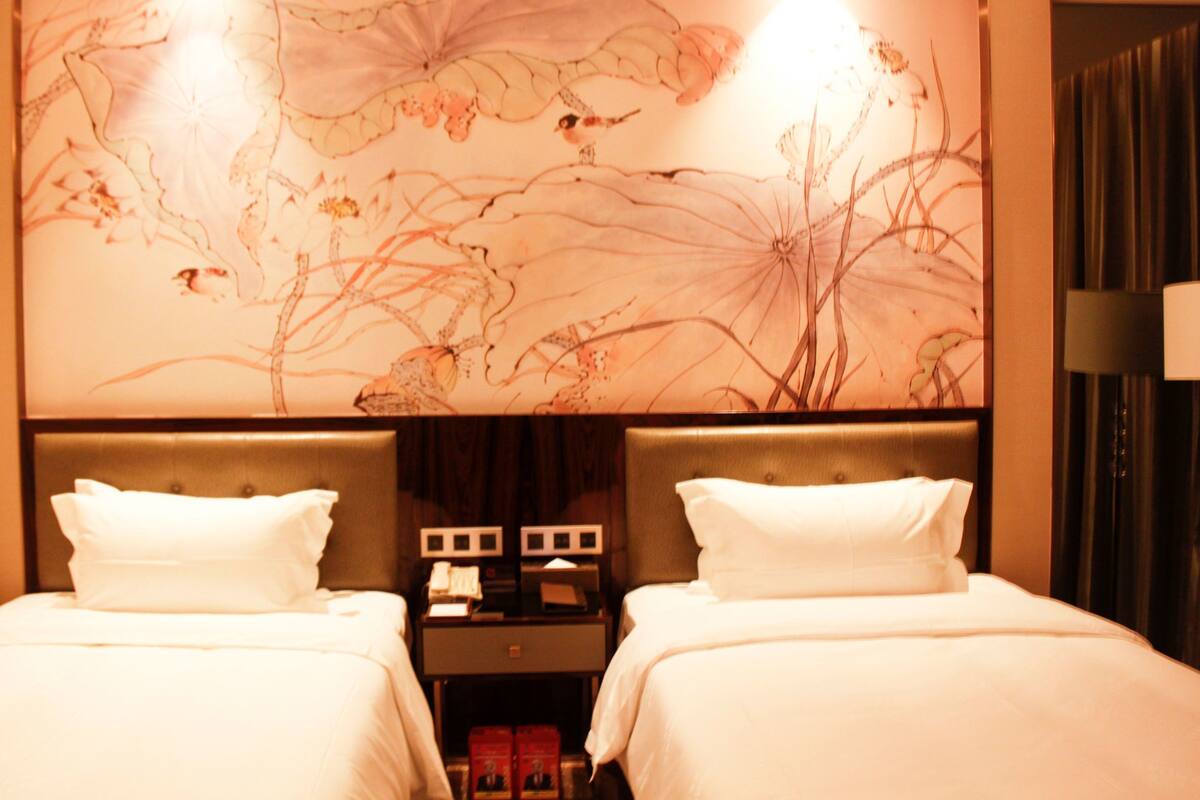 A hotel room with two beds, a nightstand with a lamp, and a floral wall mural.