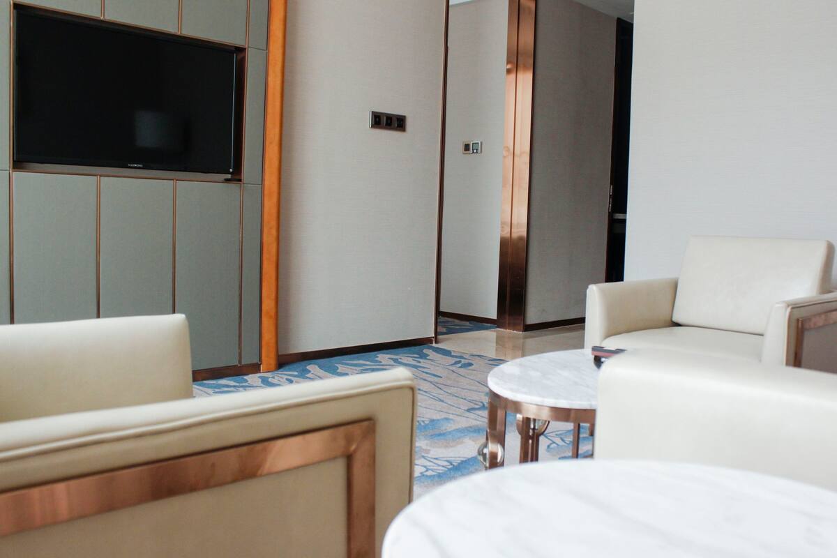 A hotel room with a flat-screen TV, a sofa, a round coffee table, and a patterned rug.