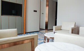 A hotel room with a flat-screen TV, a sofa, a round coffee table, and a patterned rug. - VANHONG Hotel (Guangzhou)