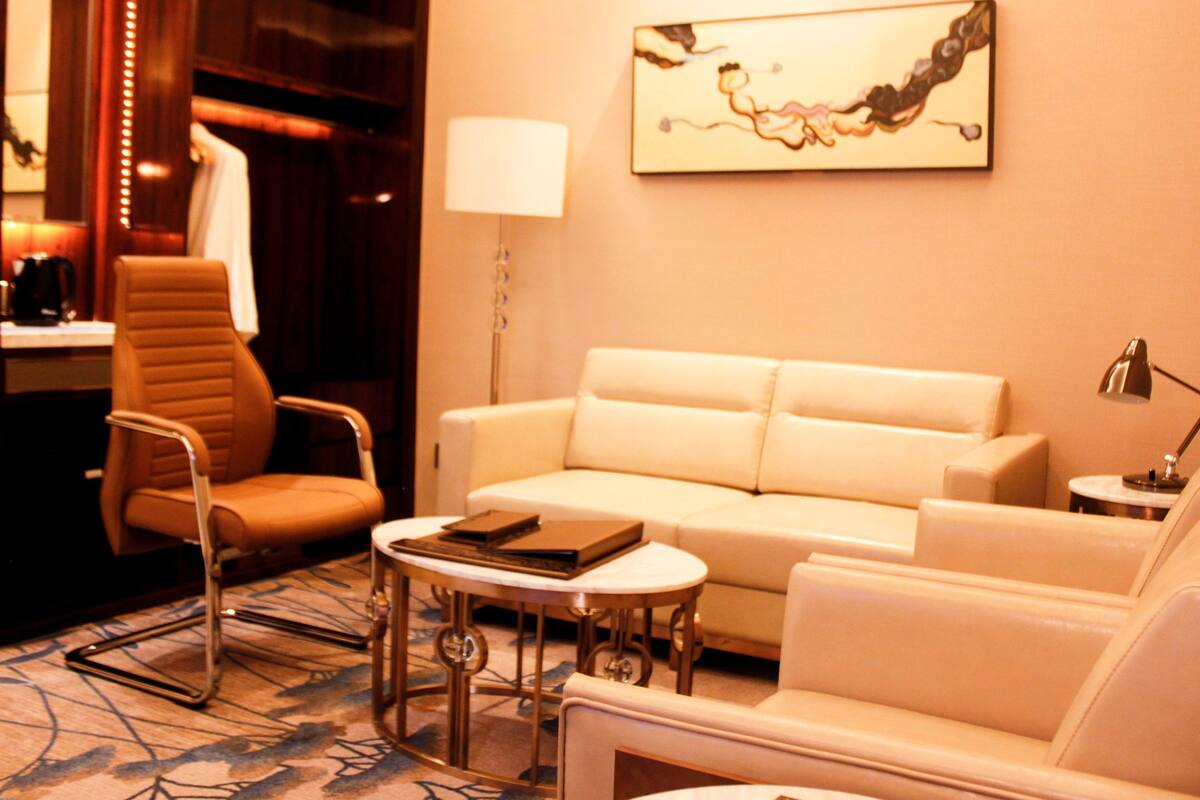 A hotel room with a white sofa, a brown armchair, a small round table, and a lamp.
