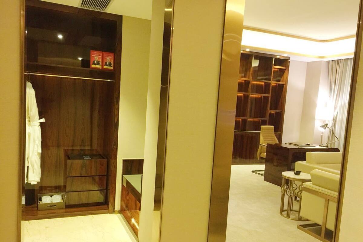 A hotel room with a walk-in closet, a seating area with a sofa and armchairs, and a small table with a lamp.