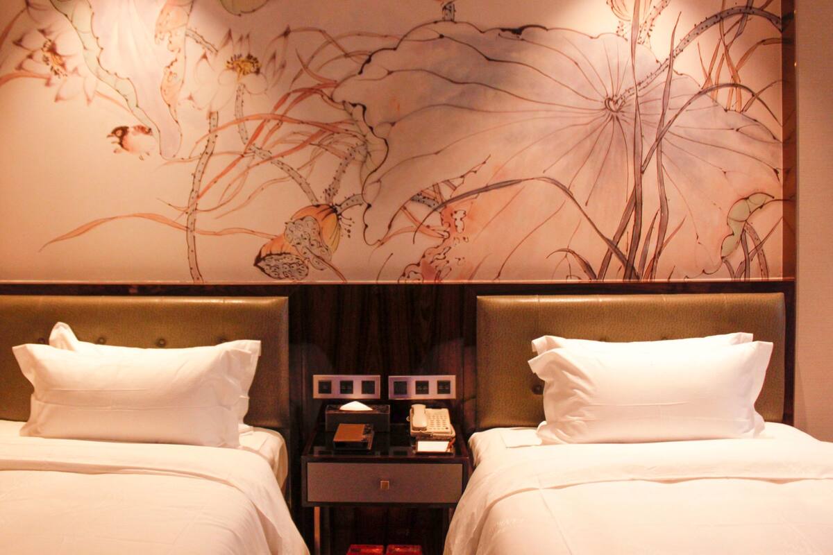 A hotel room with two beds, a nightstand with a telephone and a lamp, and a wall with a floral design.