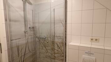 Un baño con ducha de vidrio, inodoro blanco y una toalla en el suelo.