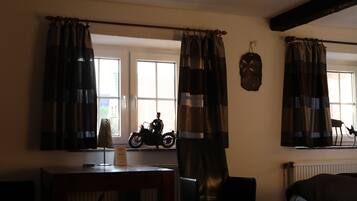 Ein Zimmer mit einem Motorrad auf einem Regal, einem Tisch mit einem Schild und Vorhängen an den Fenstern.