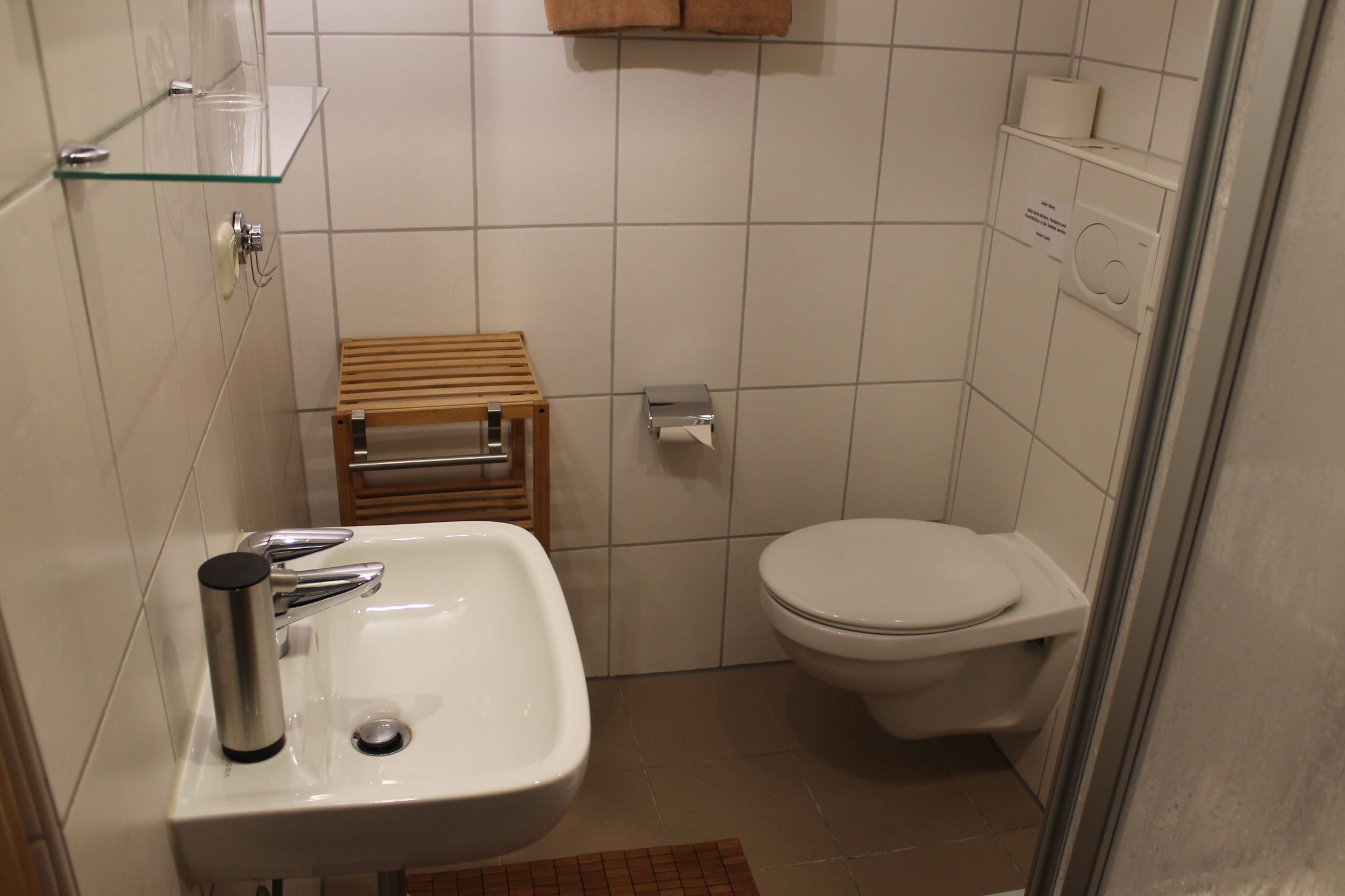 A small bathroom with a white sink, a toilet, and a glass shelf.