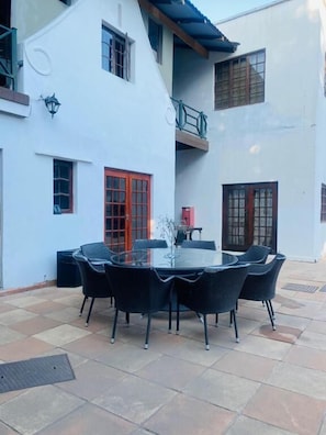An outdoor patio with a round table and chairs, a red door, and a white building with balconies.