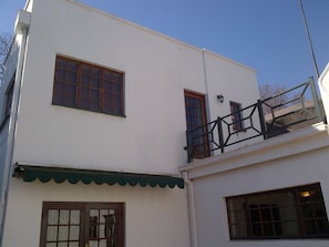 A two-story building with a balcony, a green awning, and a window with shutters.