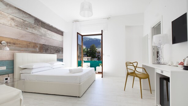 Une chambre moderne avec un grand lit, un bureau et une chaise. On peut admirer la vue sur l’extérieur à travers une porte ouverte.