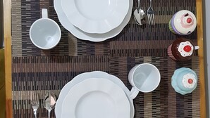 A dining table set with plates, cutlery, and a cup, surrounded by chairs. - Aorta Your Home in The Heart of EDSA (Mandaluyong)