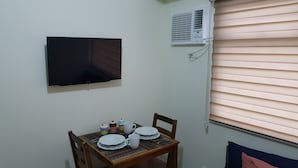 A small dining area with a table set for two, a flat-screen TV mounted on the wall, and an air conditioning unit above the window. - Aorta Your Home in The Heart of EDSA (Mandaluyong)