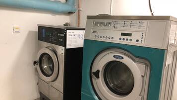 Two front-loading washing machines in a laundry room with a visible control panel and a blue pipe on the wall.
