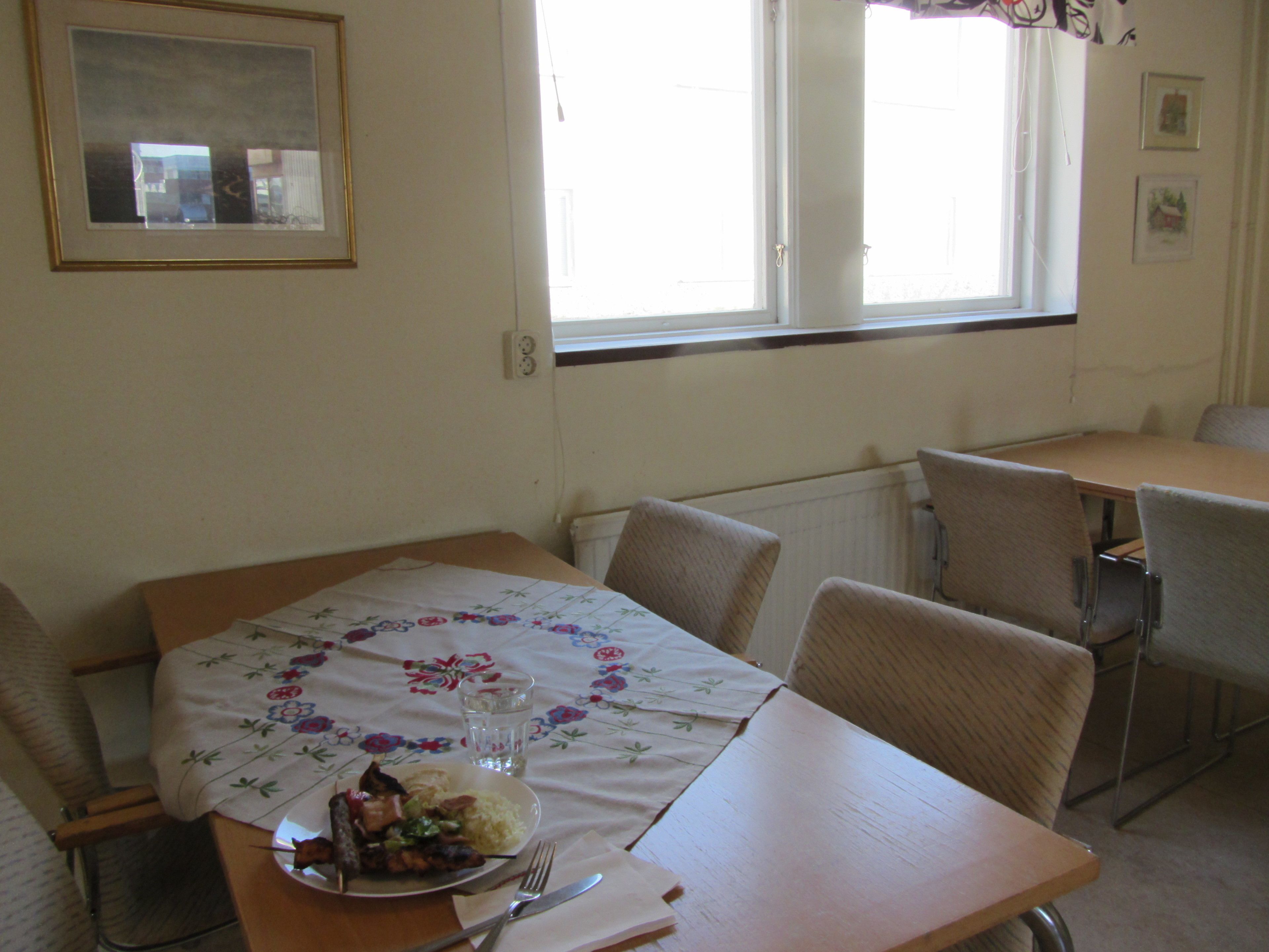 A dining area with a table set for two, a framed picture on the wall, and a window with curtains.