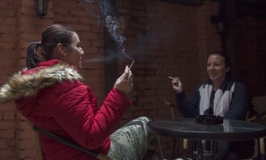 A person in a red jacket with a fur-lined hood sitting at a round table with a black tray. - Hotel Club Trio (Ostrava)